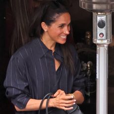 Meghan Markle wearing a navy blue pinstripe shirt and matching pair of pants with a black Loro Piana bag while eating lunch at Tre Lune in Montecito with Serena Williams.