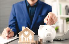 A businessman inserts a coin into a piggybank on his office desk. 
