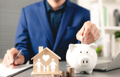 A businessman inserts a coin into a piggybank on his office desk.