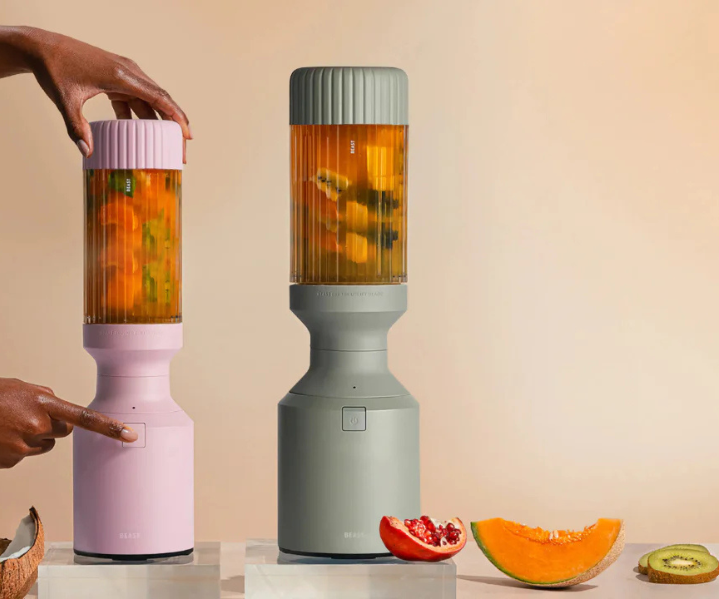 Two Beast blenders in mint and pink, blending tropical smoothies against a pale orange background