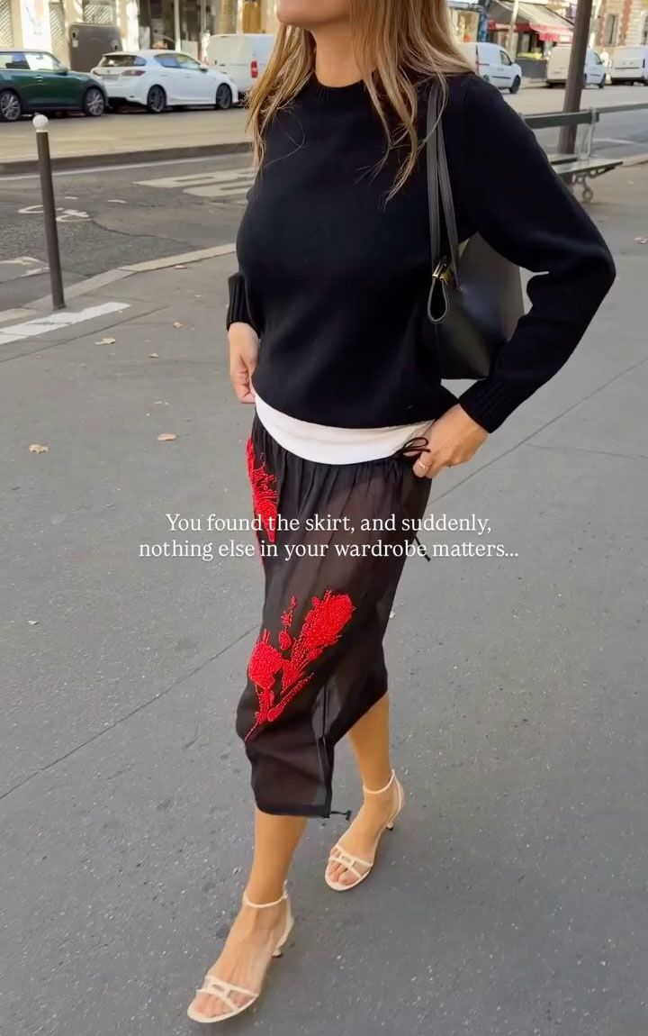 Woman in a sheer red embroidered skirt and a sweater.