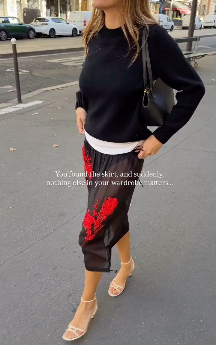 Woman in a sheer red embroidered skirt and a sweater.