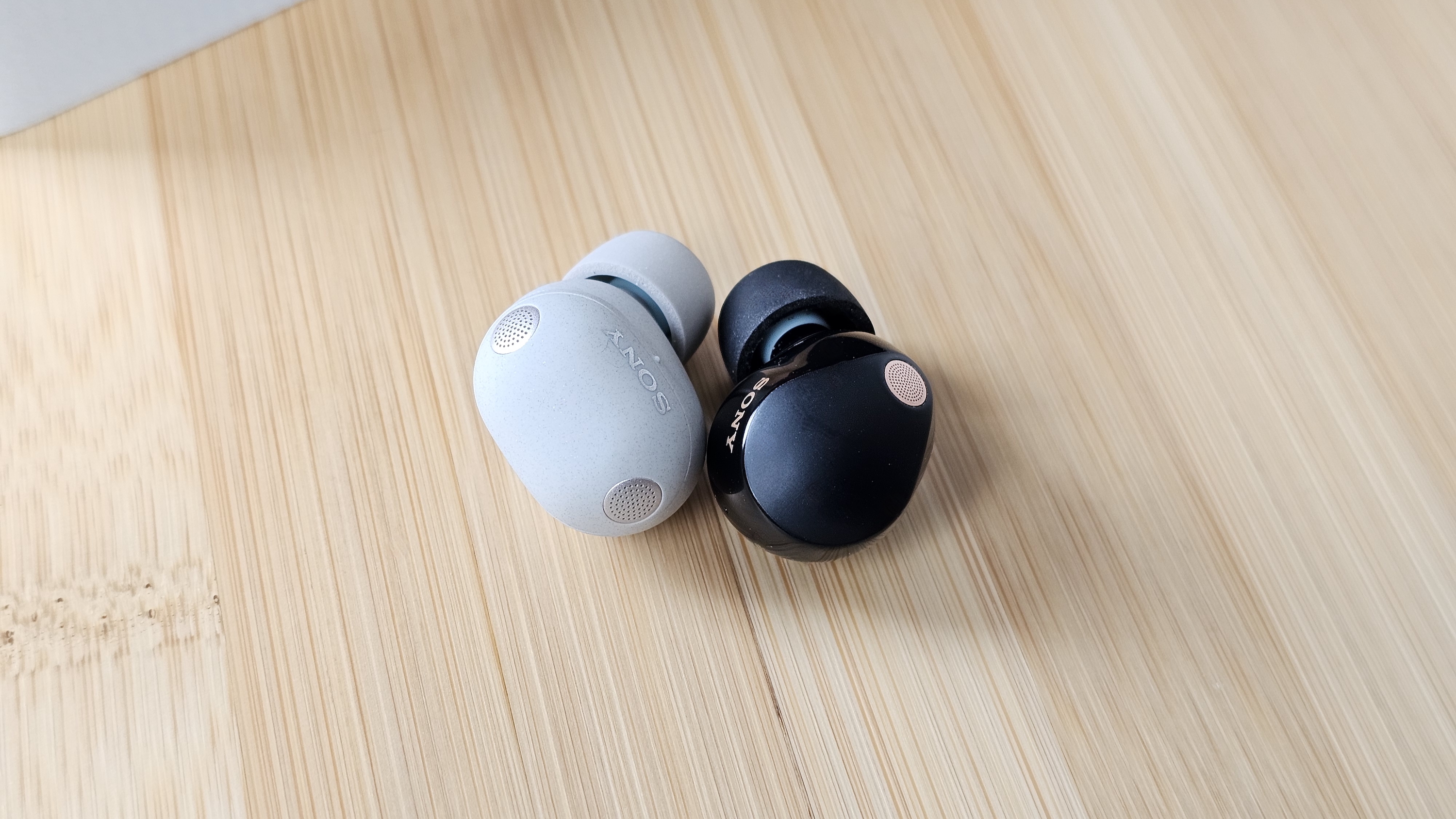 The Sony WF-1000XM6 and WF-1000XM5 side by side in a comparison, on a light wood table 