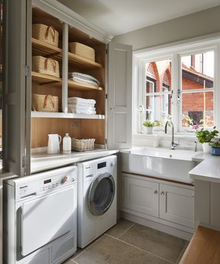 Bifold laundry room door ideas in a small neutral space with a butler sink below a window, a washing machine and pale gray stone flooring.
