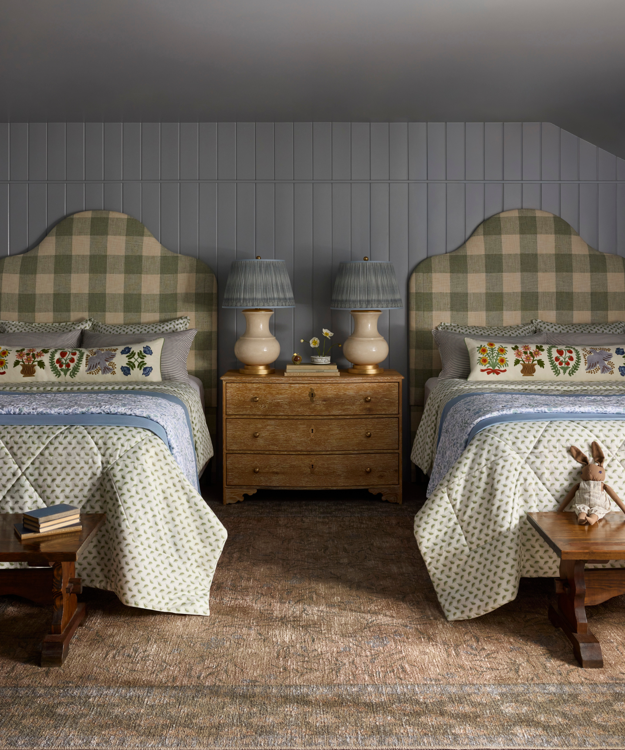 a room with twin beds, a neutral carpet, gingham headboards, printed bedspreads, and decorative pillows
