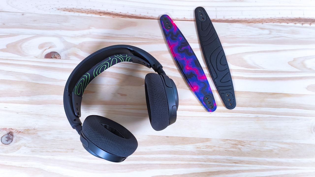 The SteelSeries Arctis Nova 5X in black on a wood table next to two extra suspension headbands