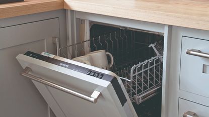 An open dishwasher in a light grey kitchen with silver hardware