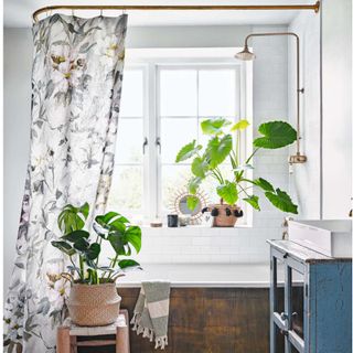 Bathroom with white tiles, basin on blue vintage cupboard, bathtub under window and white shower curtain with botanical pattern
