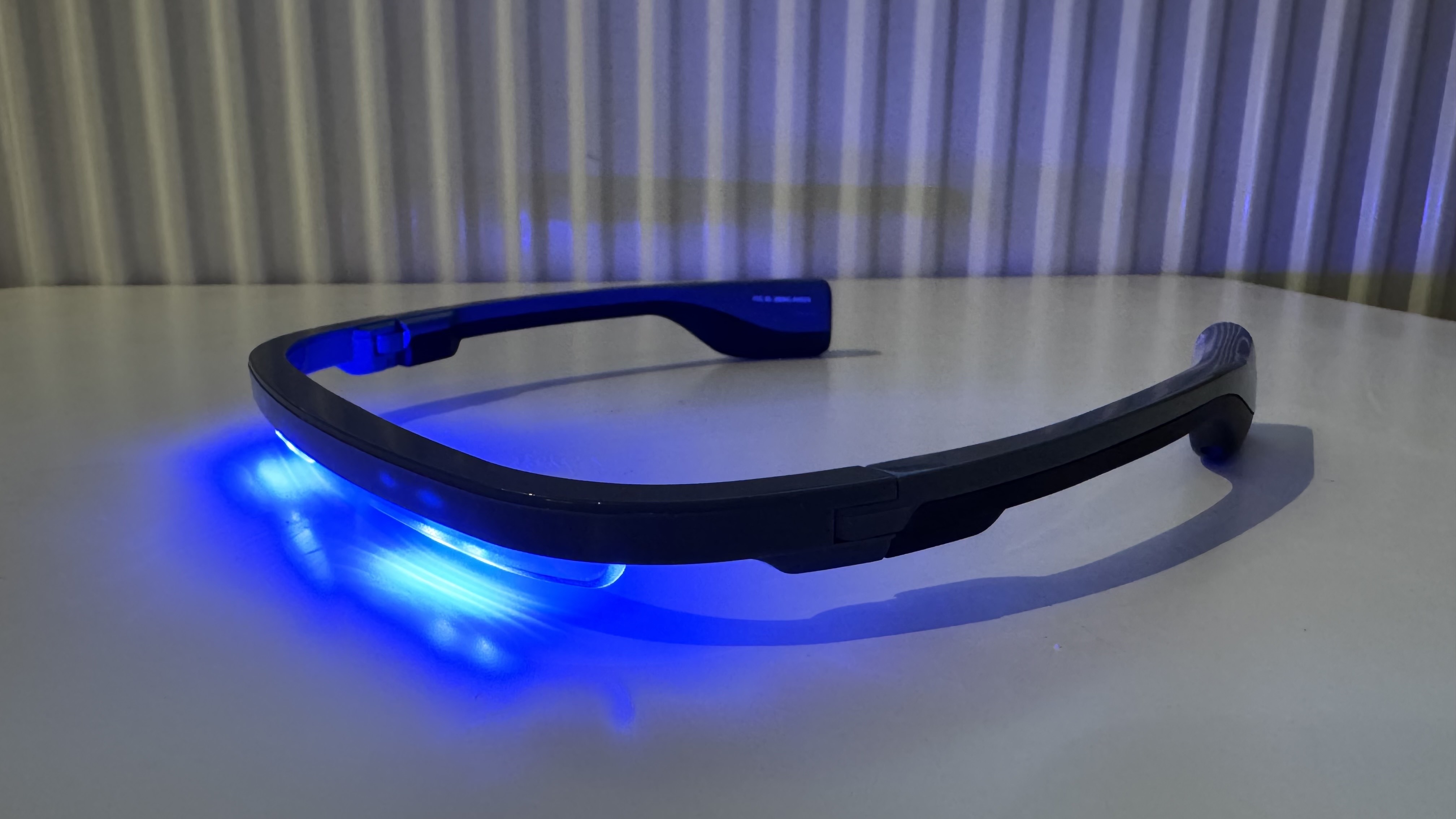 The AYO+ Blue Light Therapy Glasses placed on a white wooden, highly reflective surface