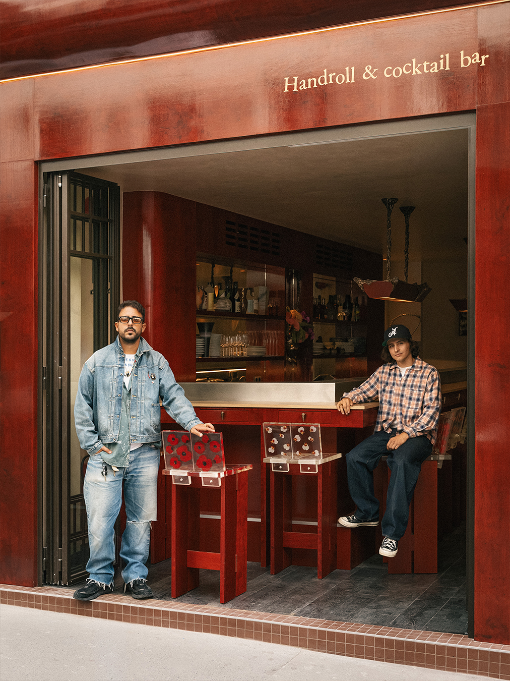 A red-painted wood and chrome bar of a restaurant, decorated with tall, geometrically cut wooden stools with flower-decorated resin backs.