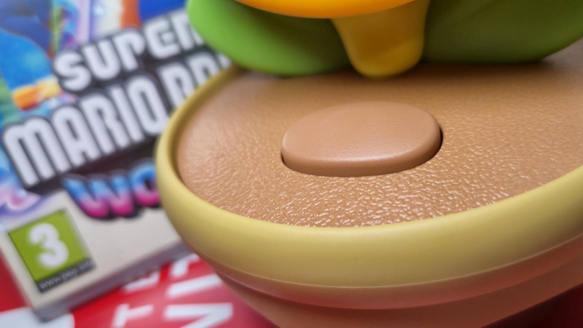 Close up of the Talking Flower button with a copy of Super Mario Bros Wonder in the background.