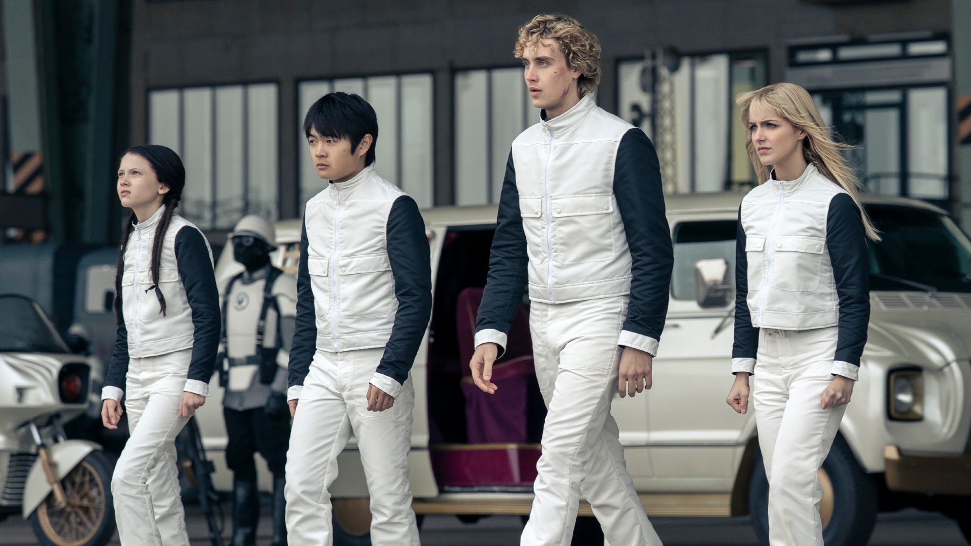 Four members of the cast of The Hunger Games: Sunrise on the Reaping walking together in white uniforms.