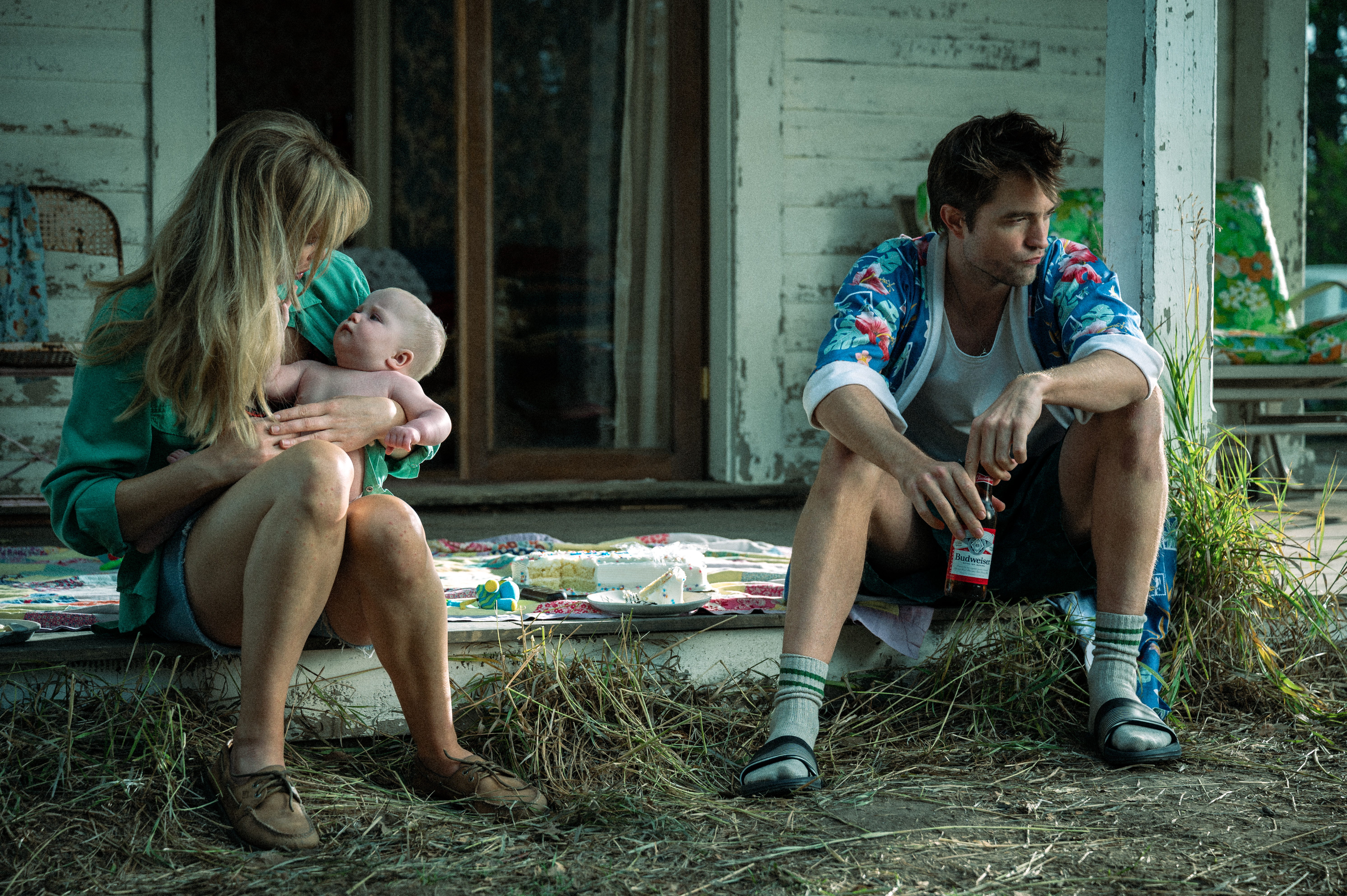 jennifer lawrence in die my love holding a baby and sitting on the front stoop of her home with her husband played by robert pattinson