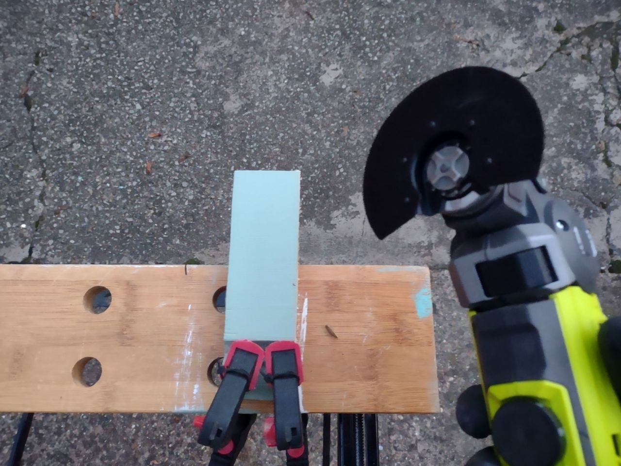 A multitool with a cutting attachment being used to cut a piece of wood