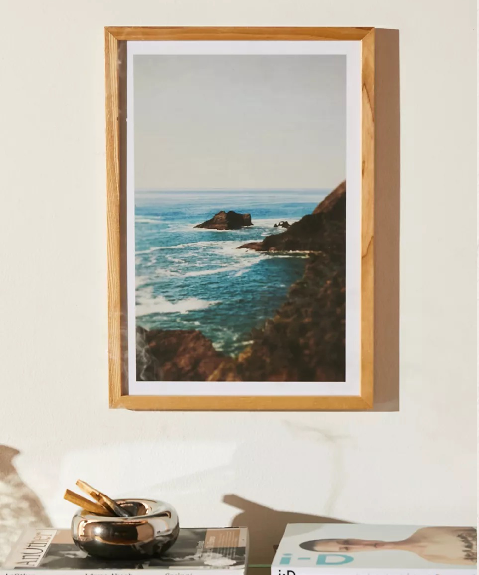 A coastal art print in a wooden frame above a shelf
