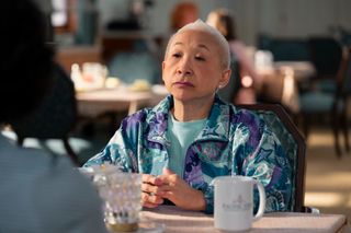 Lori Tan Chinn as Susan, sitting with her hands crossed at a dining room table, in episode 105 of 'A Man on the Inside.'