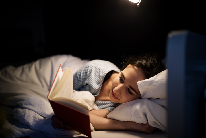 A woman laying on her side in bed reading a book