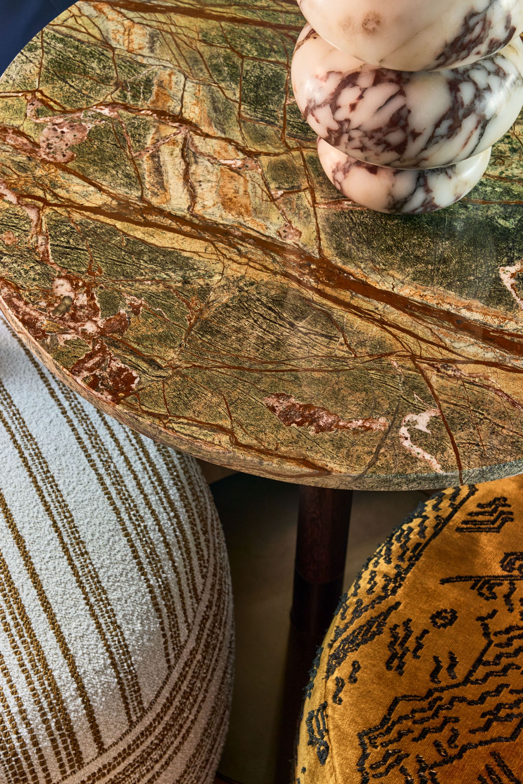 Close up of a green marble table with two patterned stools under it.