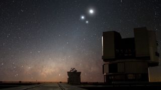 Image of three bright points of light in the sky above ground-based telescopes.