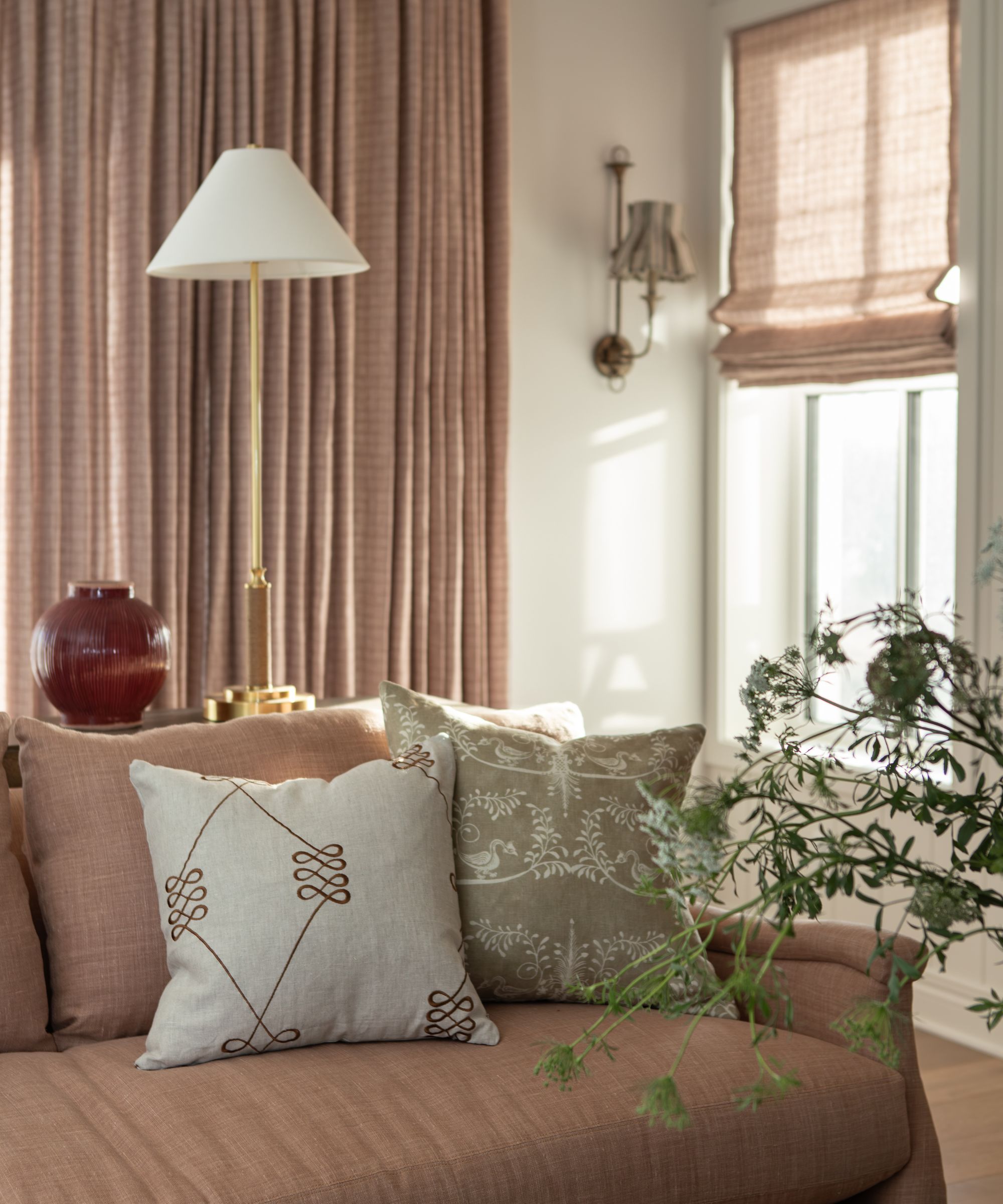 a cozy neutral corner of a living room with pink sofa, drapes and blinds and patterned pillows