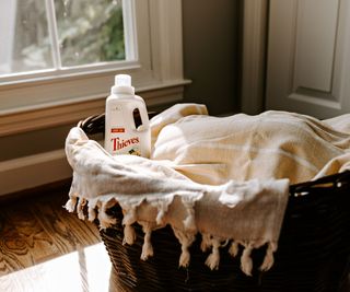 A wicker laundry basket filled with clothes and a laundry detergent bottle