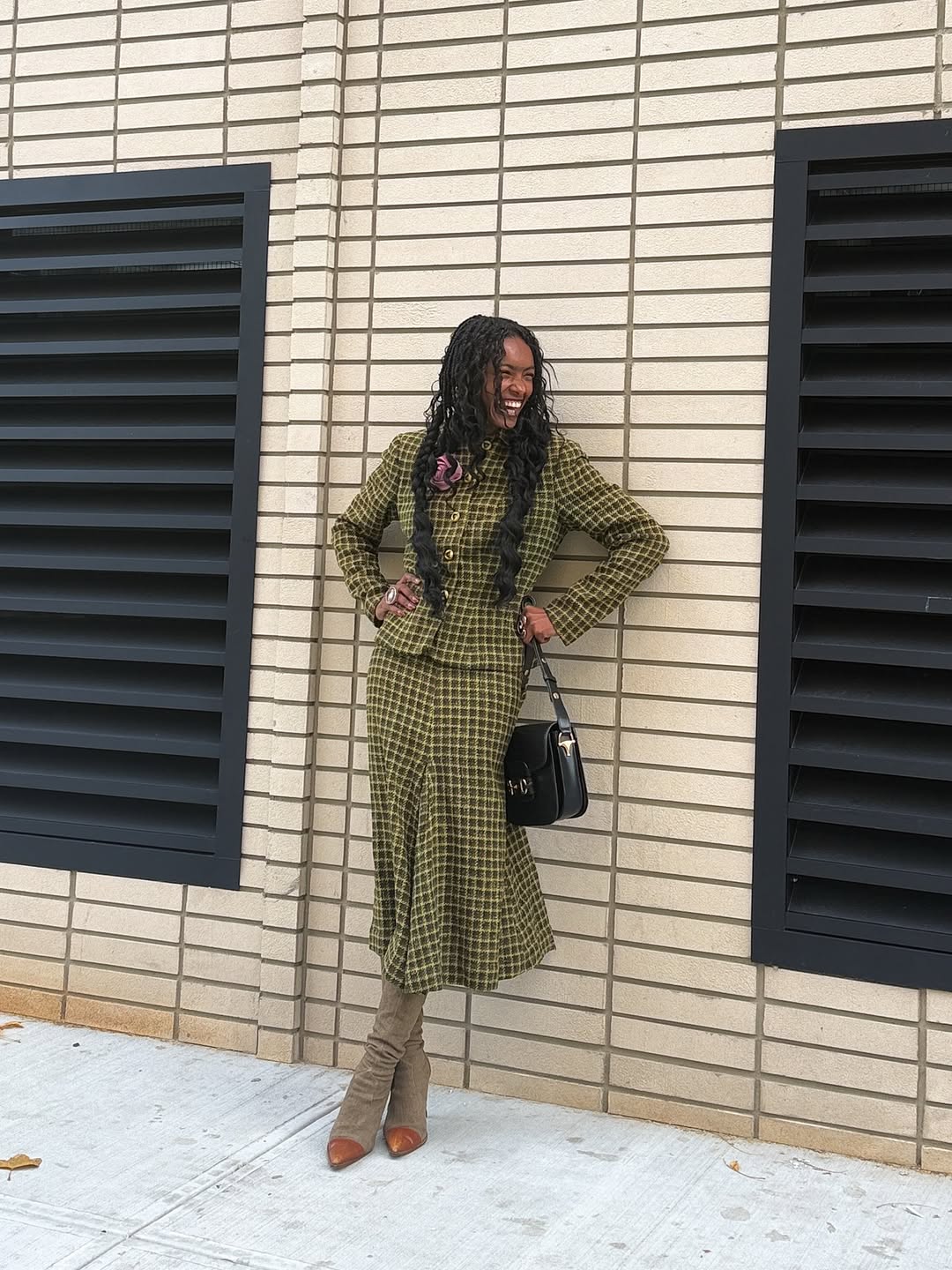 A woman wears a green skirt suit with brown cap-toed boots.