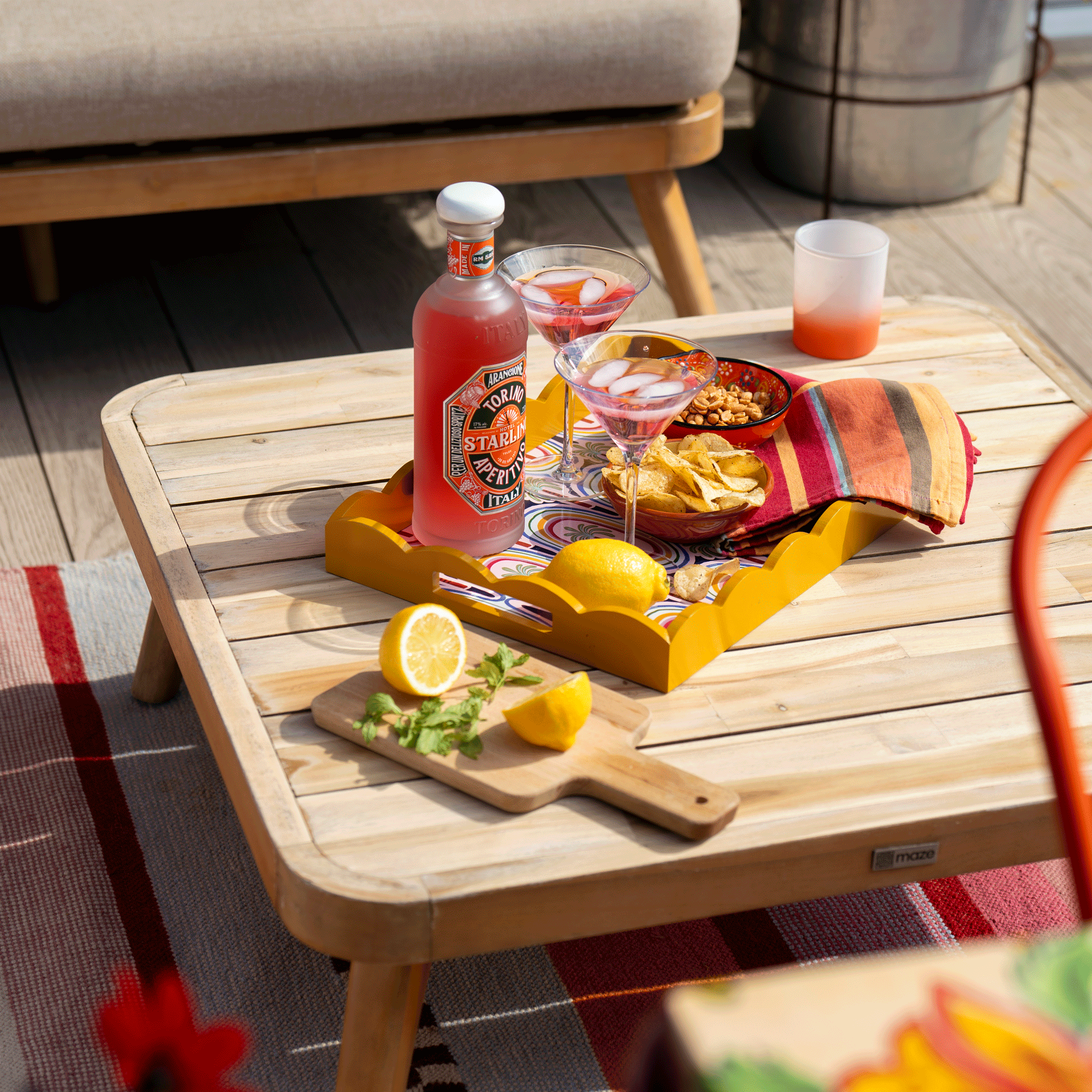 a yellow tray on a low wooden coffee table with cocktail glasses and a chopping board with lemons and mint