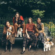 Four models outdoors on a park bench with small terrier dogs, wearing preppy, autumn Boden fashion including plaid and corduroy trousers, trench coats, knits, and leather boots.