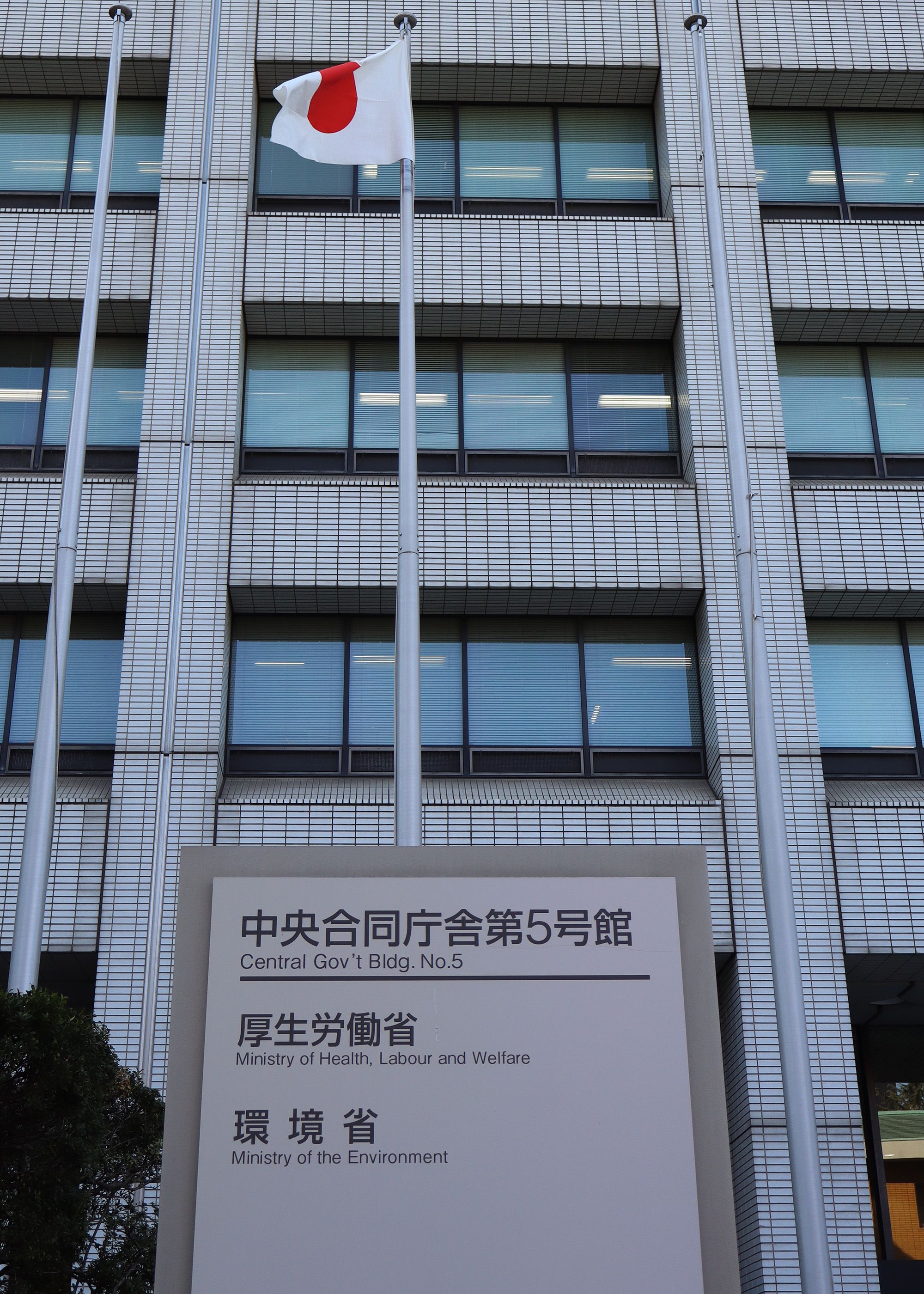 A building with a Japanese flag flying in front of it and a plaque with both English and Japanese writing on it