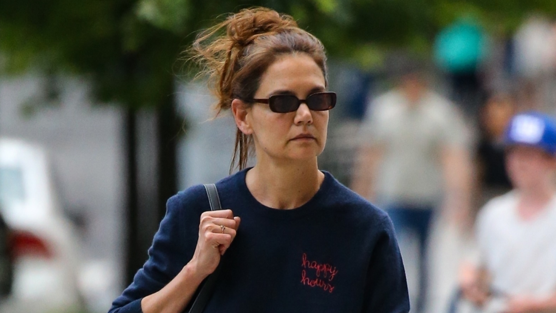 Katie Holmes carries a black Khaite bag and wears a navy sweatshirt featuring the words Happy hours