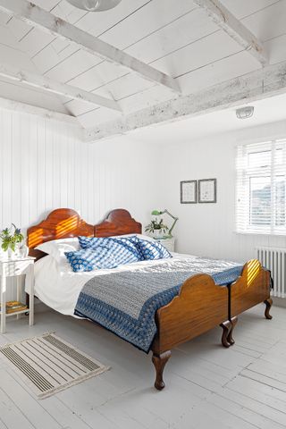 white bedroom with shiplap paneling, gray wood flooring and a wooden bed