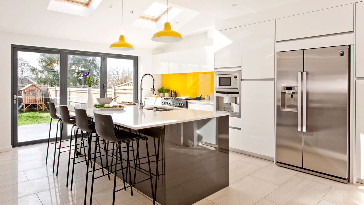 Smart stainless steel American style fridge freezer in a white kitchen with yellow glass splashback