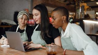 Three women browsing laptop in cafe