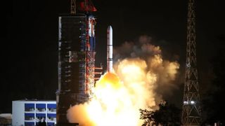 a white rocket launches at night, creating a large plume of exhaust lit orange by its engine fire.