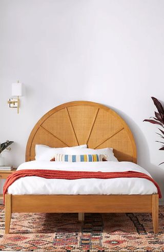 Bedroom with wooden bedframe, rounded headboard, boho style, white bedding, accent cushions and throws