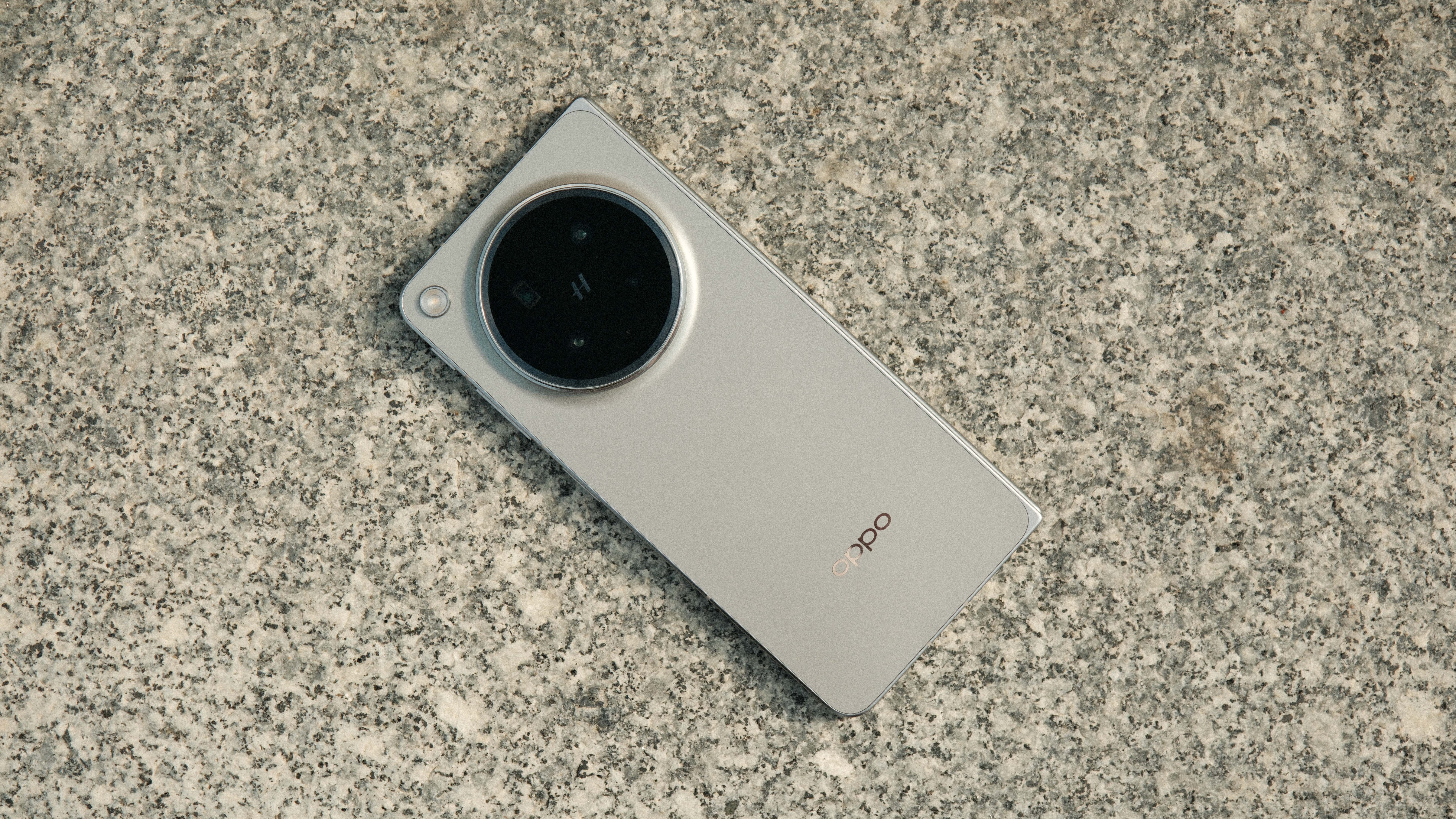 A top-down view of the Oppo Find N6 lying flat on a textured grey stone surface, showcasing the minimalist design of the rear glass and the prominent circular camera island.
