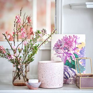 Glass vase of flowers beside a picture of a flower on a grey shelf