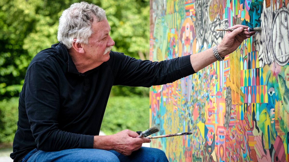 Man paints a design on a wall outside.