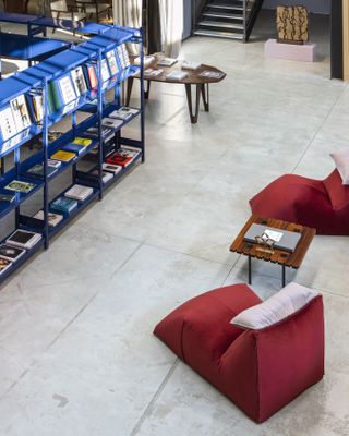 Interior of Nilufar Depot with concrete floors, blue bookcases on the left and red velvet lounge chairs on the right