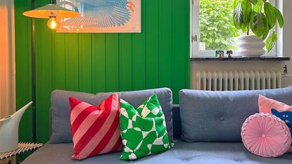 A gray couch with colorful cushions next to a green wall and window