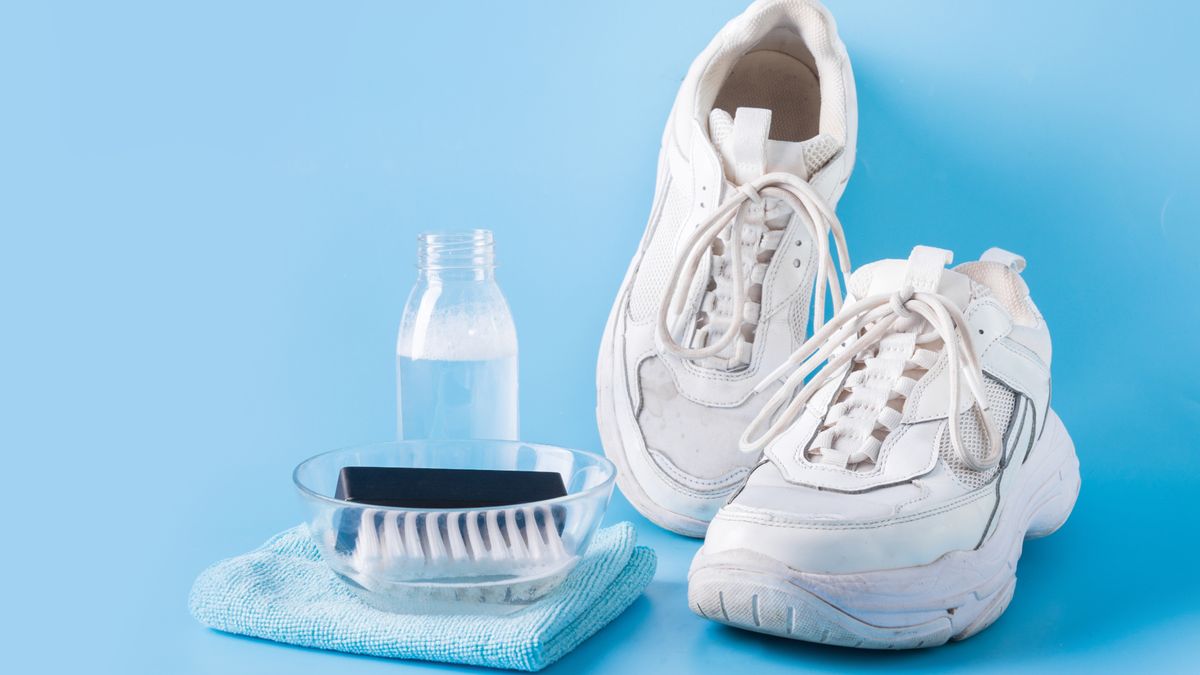 Dirty white sneakers with special tool for cleaning them on blue