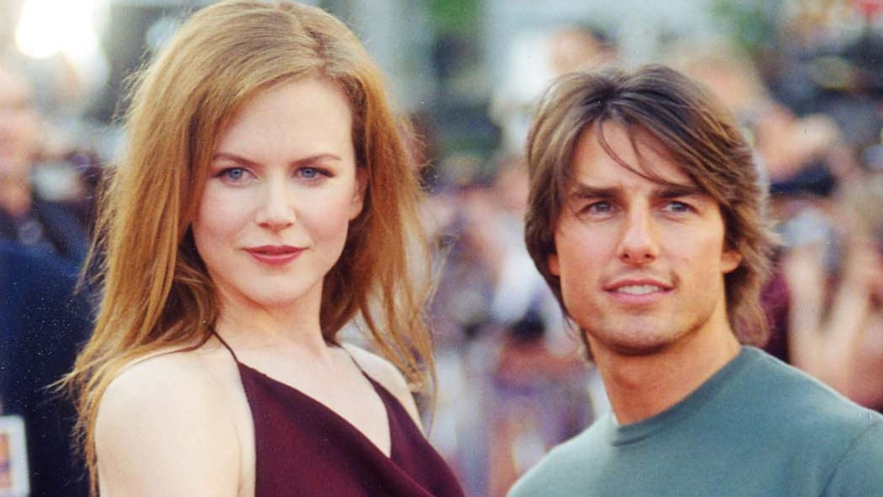 Nicole Kidman wears a strappy red top and long ginger hair as she poses with her then-husband Tom Cruise who wears a blue sweater