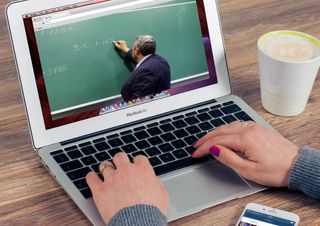 An open laptop shows a video of a teacher writing on a chalkboard