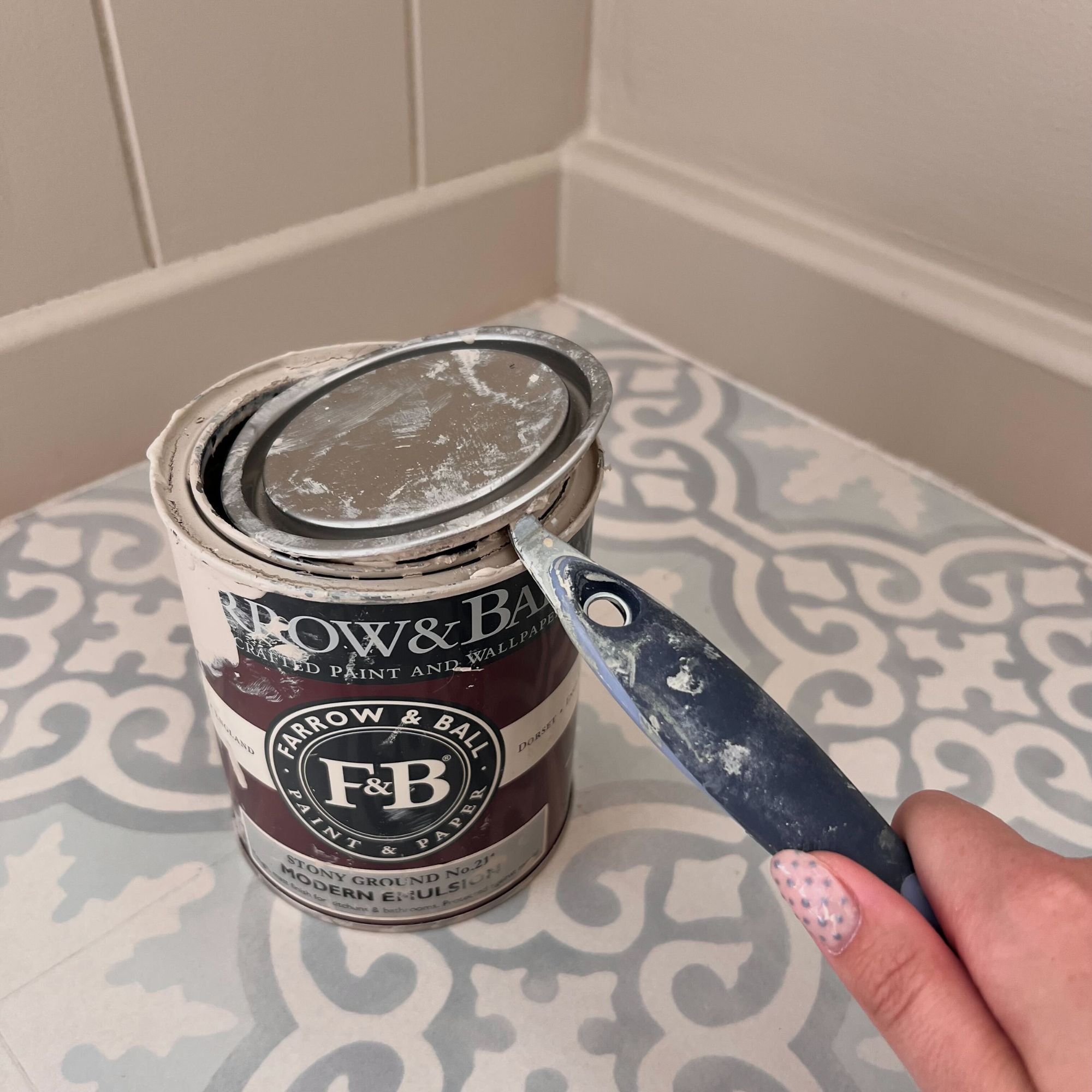 A hand using the Dulux Perfect Finish paint brush to open a tin of Farrow & Ball paint.