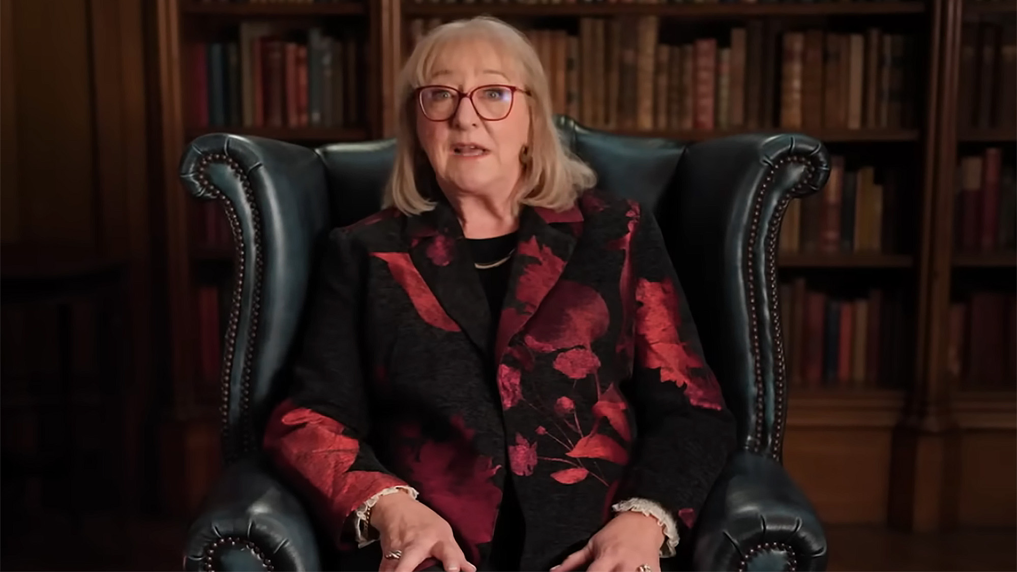 Mamma Donna in a red and black blazer sitting in a chair for an interview on The Traitors.