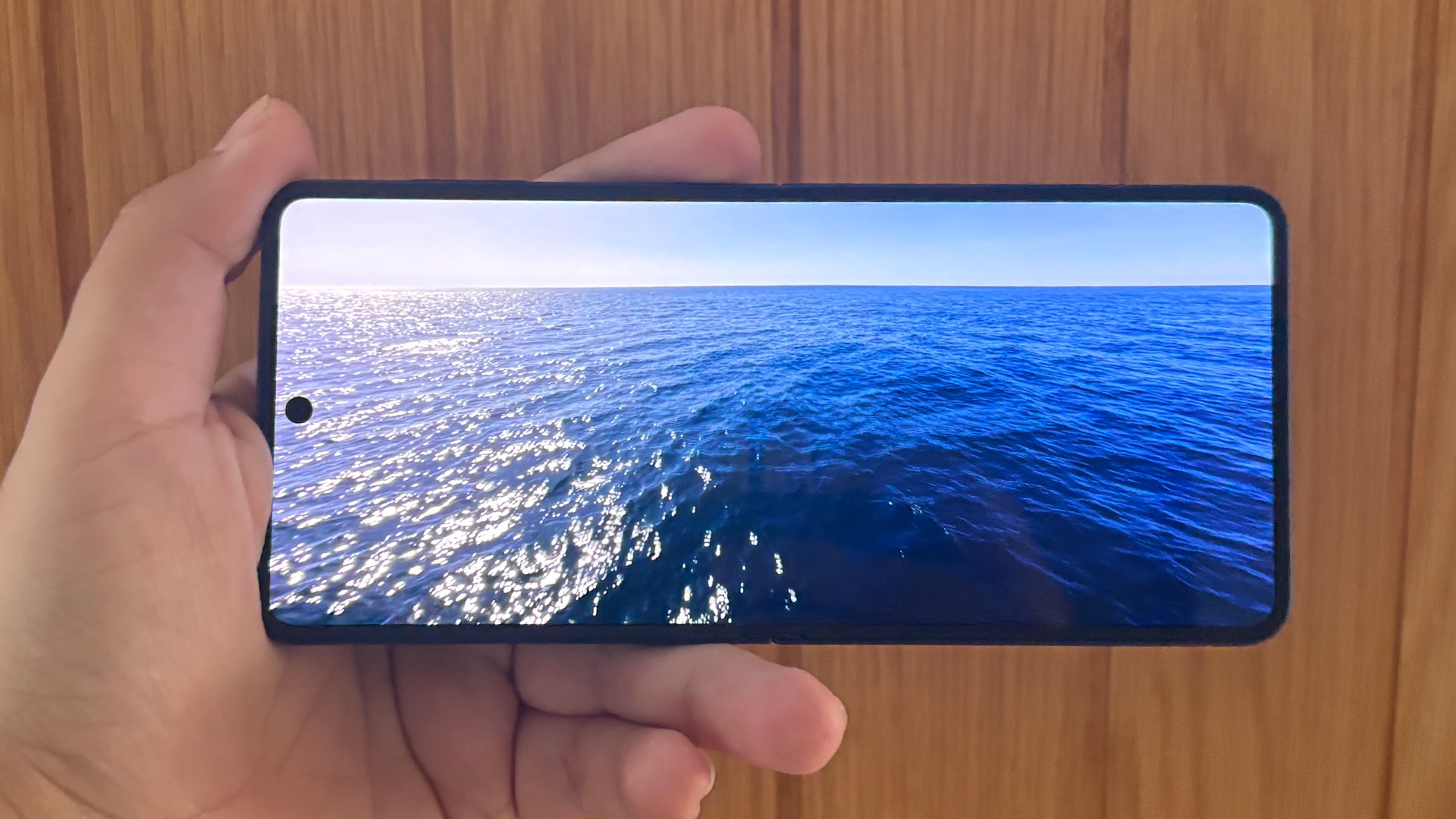 Samsung Galaxy Z Flip 7 smartphone held in hand with phone open showing ocean on screen