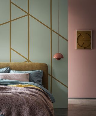 Contemporary bedroom with green and gold geometric feature walls, pink painted wall in background, low hanging pink flowerpot pendant lights, dark yellow upholstered headboard with blue and pink bedding