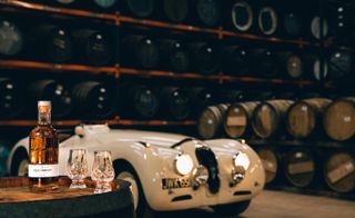 Blended Scotch whisky bottle and glasses with barrels and car in background