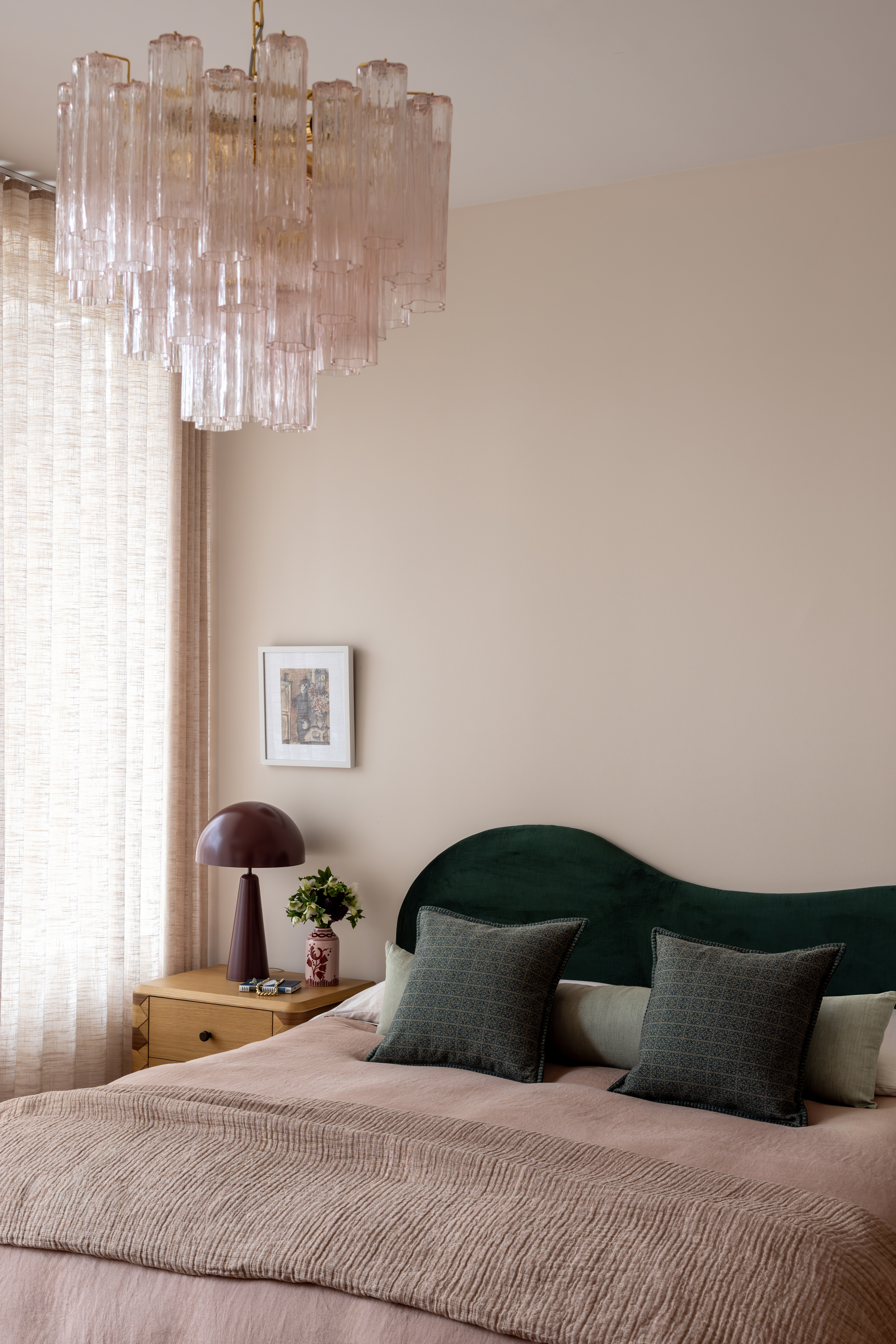 A bedroom with pink bedding, pink walls and a pink chandelier, with green headboard