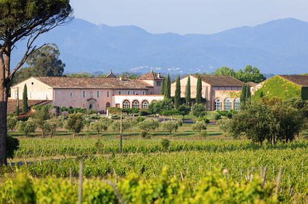 The winery, a pink building with trees in front of it, with vines in the foreground and hills in the background